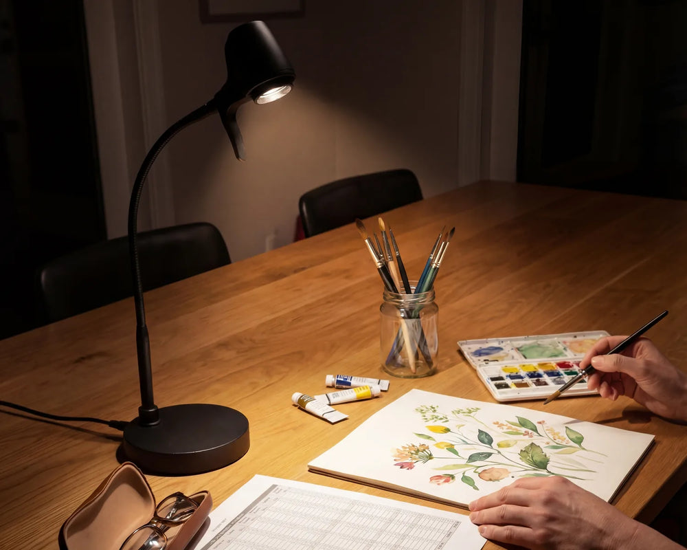 Hands painting a botanical watercolour at a table in the evening, under a Serious Light