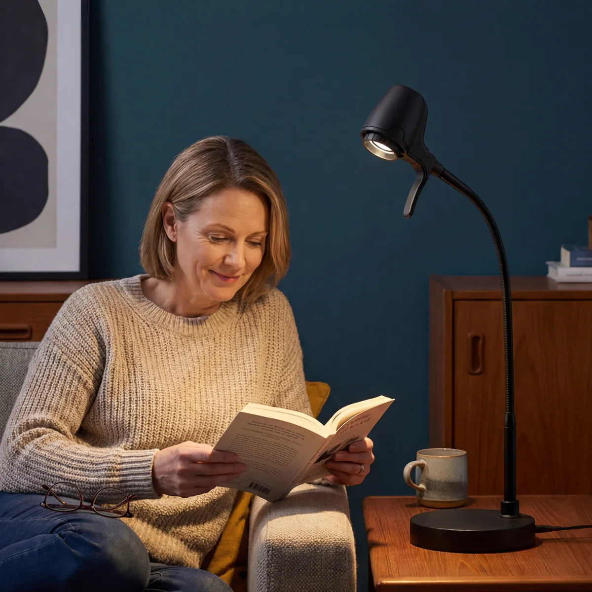 A woman reading in an armchair by the light of an HD Pro Table Light on the side table