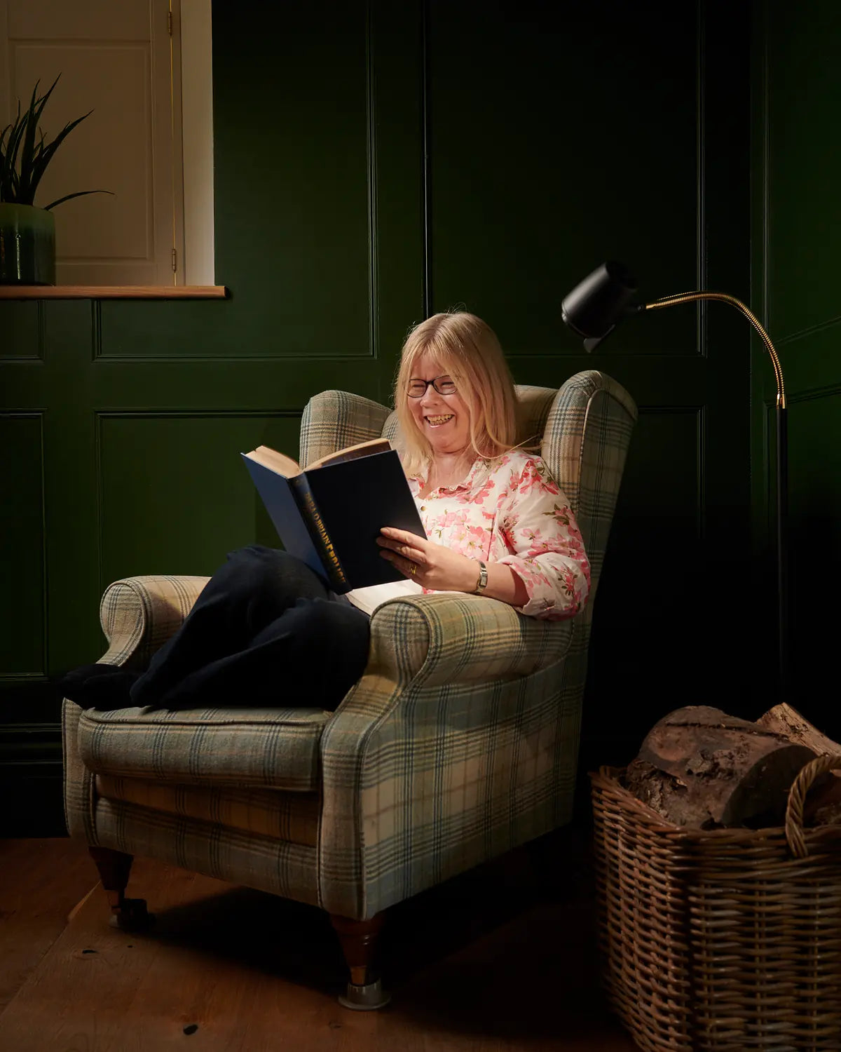 A woman reading in a tartan armchair beside an HD Original Floor Light in Black