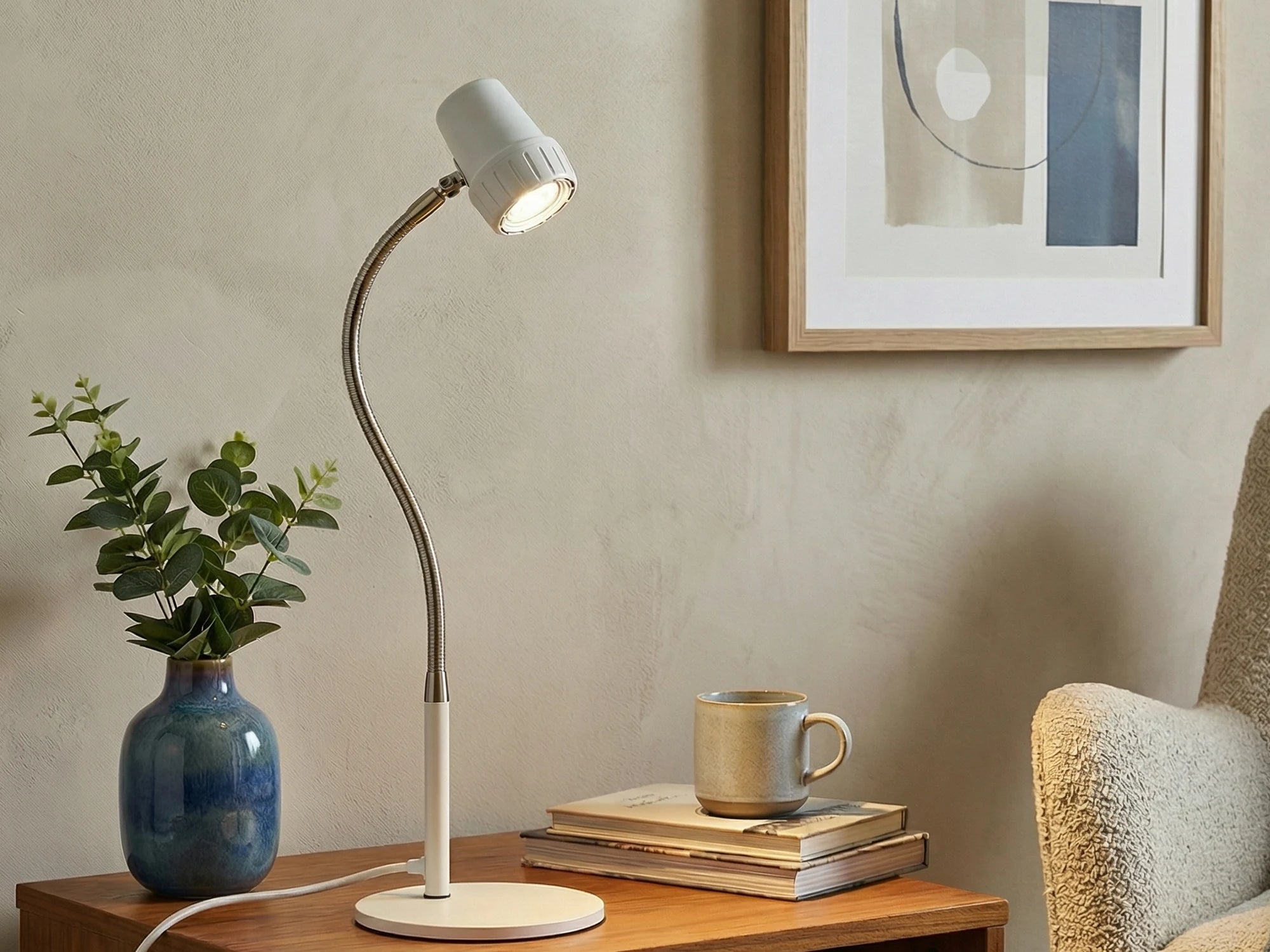 An HD Essential Table Light in Heritage White on a side table beside a vase and a pile of books