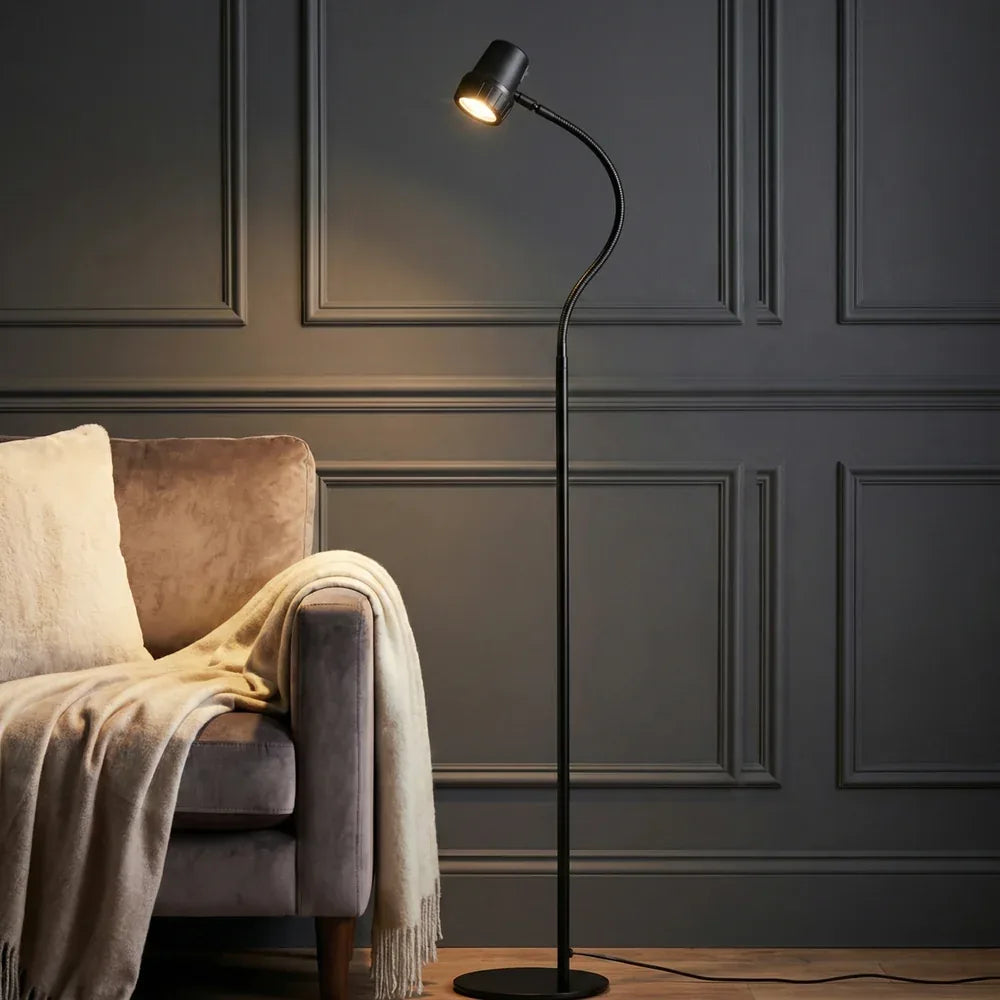 An HD Essential Floor Light in Black beside a grey velvet sofa in a panelled room