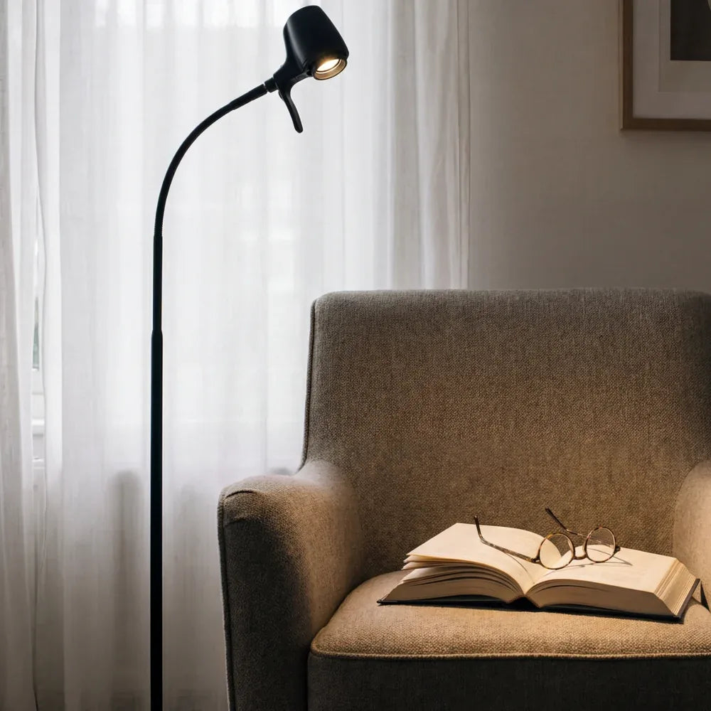 An HD Original Floor Light in Black beside an armchair, with an open book and glasses on the seat