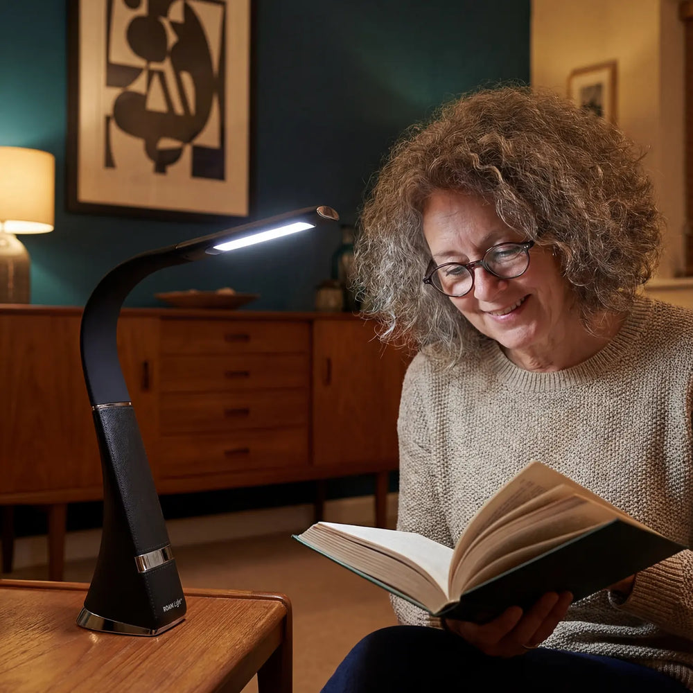 A woman reading in an armchair beside the HD ROAM in Black