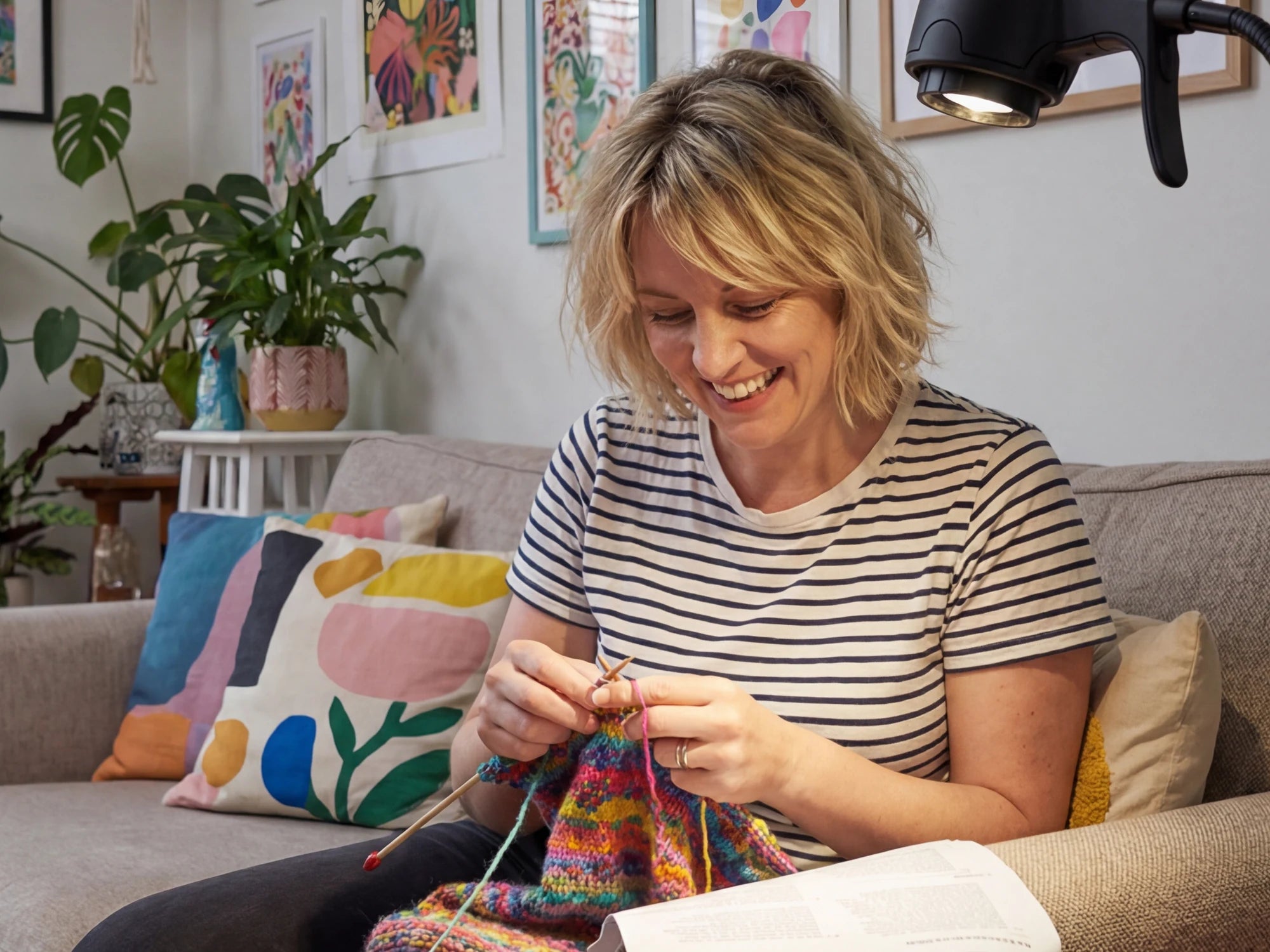 A woman laughing as she knits on her sofa by the light of an HD Pro Table Light