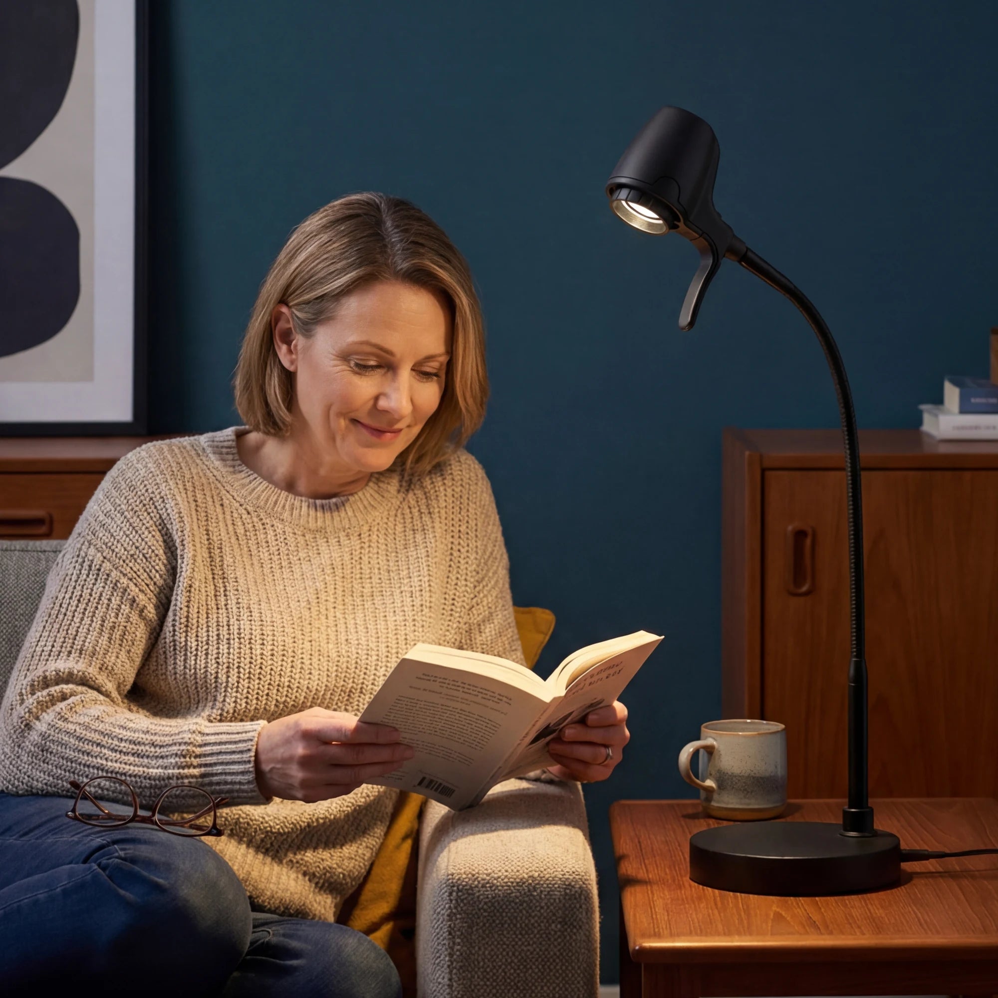 A woman reading in an armchair by the light of an HD Pro Table Light on the side table
